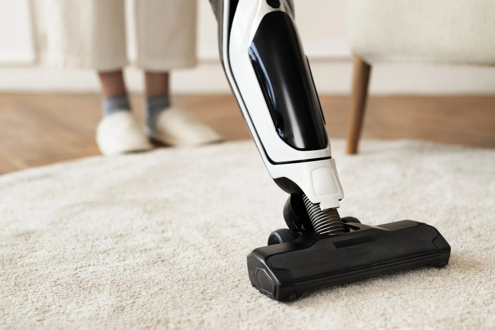 Person vacuuming a white rug with a black and white vacuum.