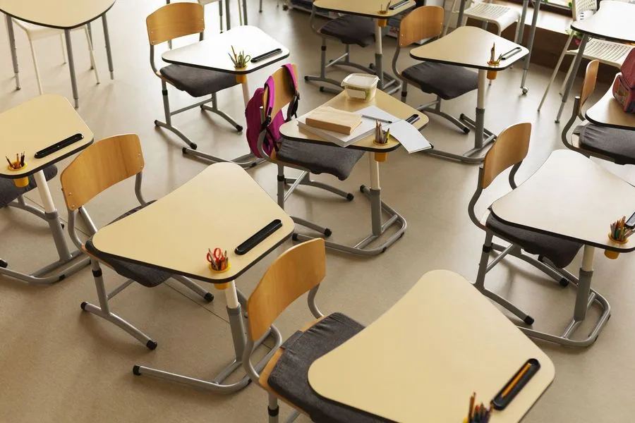 Empty classroom with angled desks and chairs. Some desks have books and supplies.