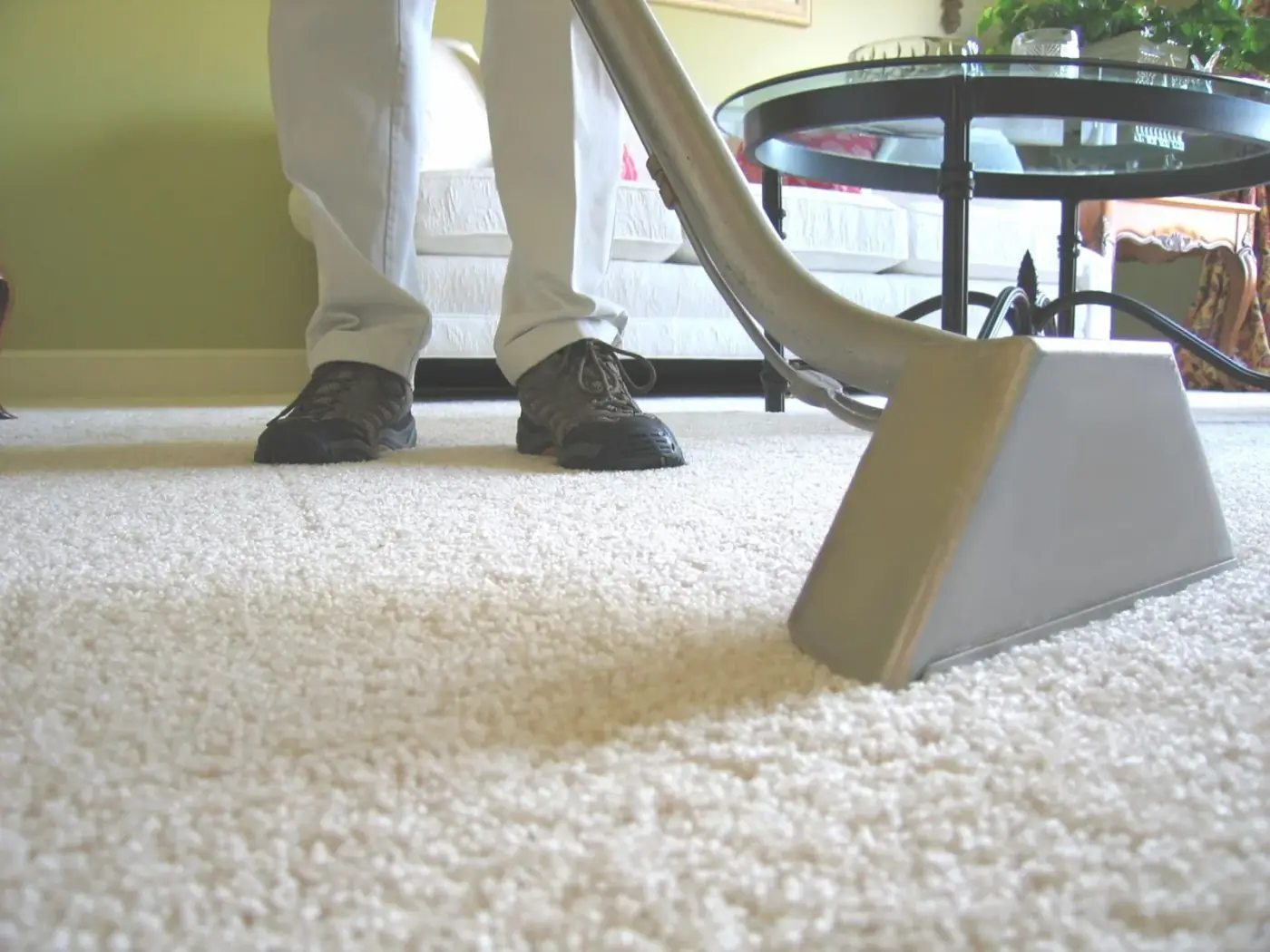 Person vacuuming white carpet with a gray vacuum cleaner.