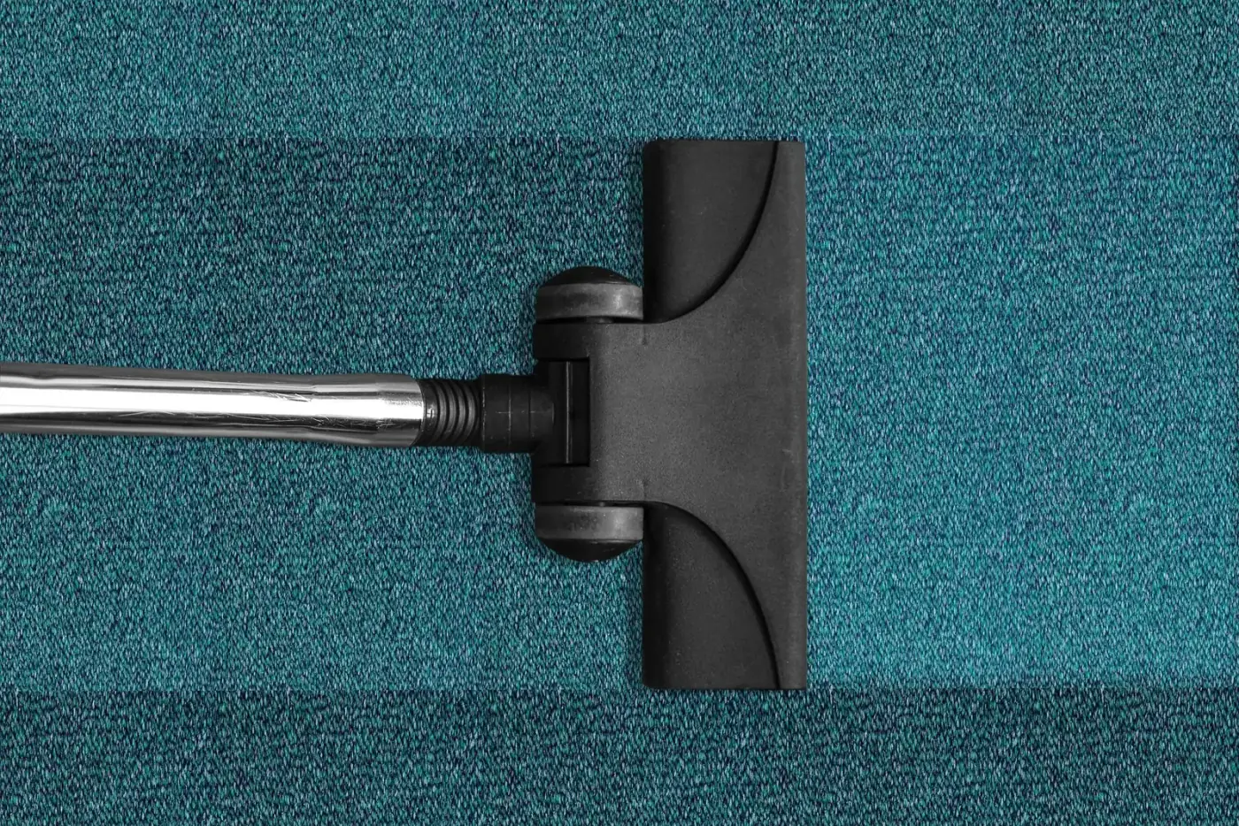 Vacuum cleaner head cleaning a teal carpet, creating a lighter stripe.